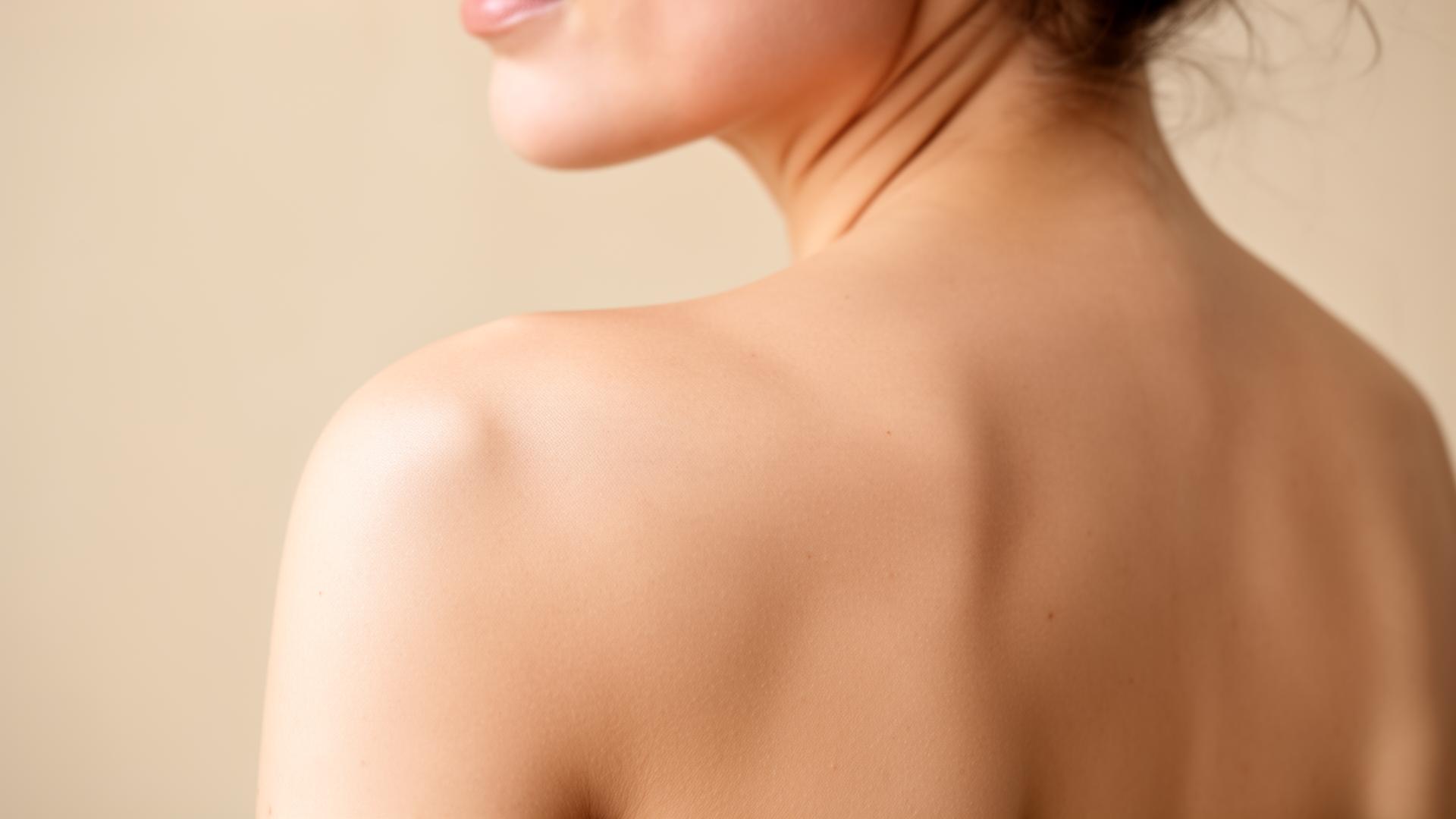 A woman's back and shoulder in soft natural light — body work and aesthetic wellness